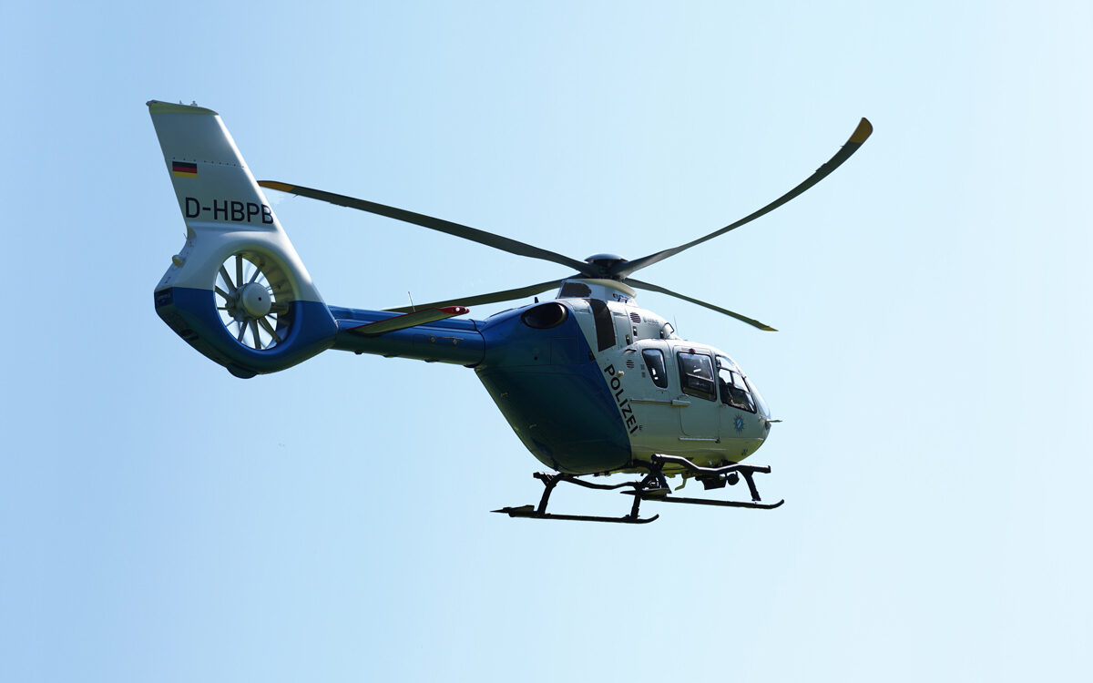 Polizei Hubschrauber bei Vermisstensuche im Einsatz im Flug vor blauem Himmel Polizei Hubschrauber bei Vermisstensuche im Einsatz im Flug vor blauem Himmel